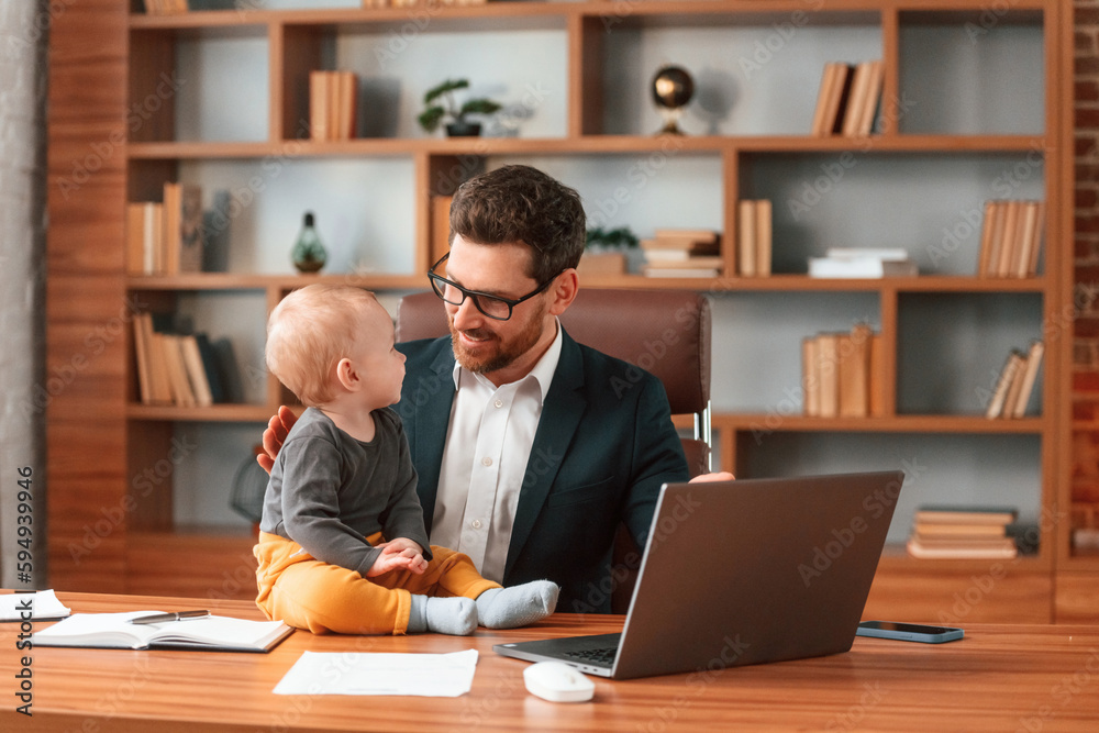 With toddler. Businessman in formal clothes is working indoors With toddler. Businessman in formal clothes is working indoors