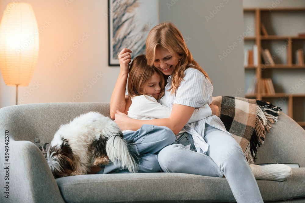 On the sofa. Mother with her daughter and with cute dog is in domestic room On the sofa. Mother with her daughter and with cute dog is in domestic room