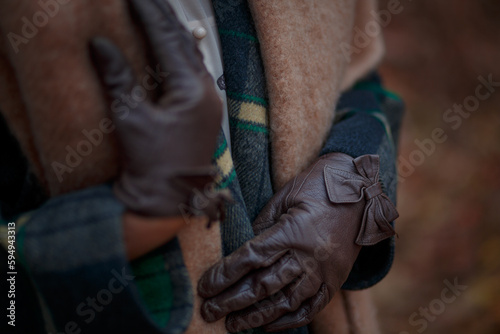 Female hands in brown leather glovesagainst the background of a terracotta woolen scarf and a plaid coat