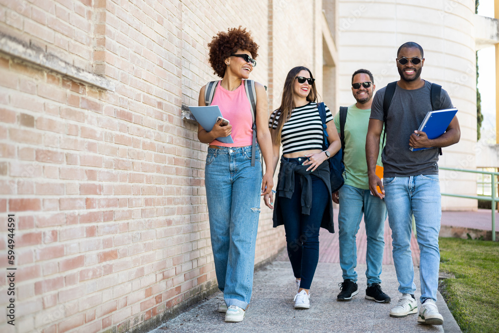 A diverse group of casually dressed college students wearing sunglasses. The 4 young people are walking around the university with textbooks and backpacks. Concept of break between classes.