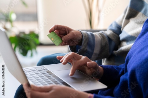 Crop anonymous women using laptop while paying online with credit card for purchases on internet remotely from home photo