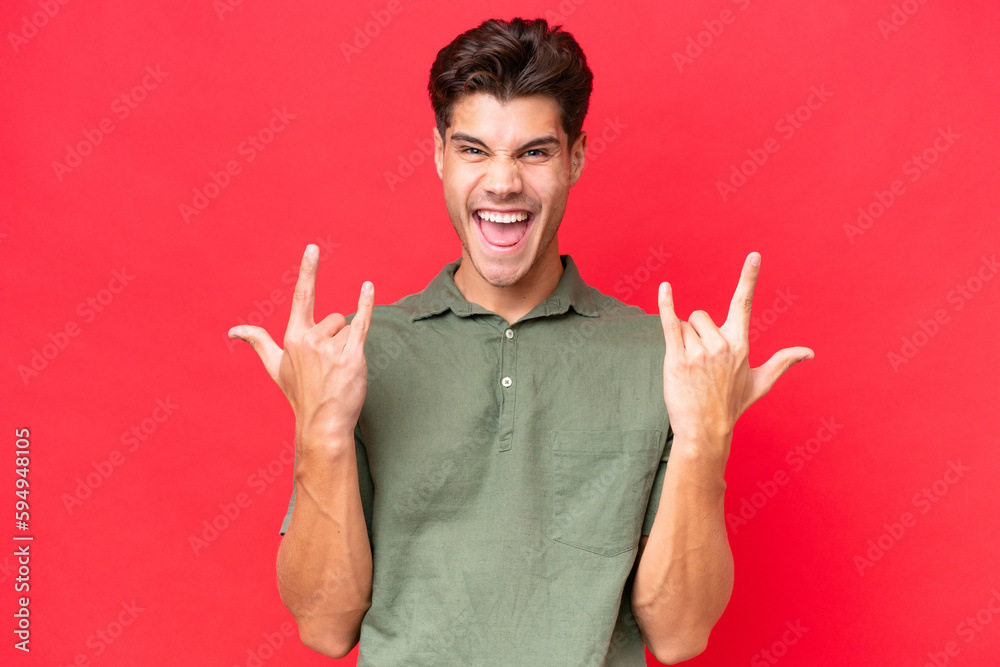 Young caucasian handsome man isolated on red background making horn gesture Young caucasian handsome man isolated on red background making horn gesture