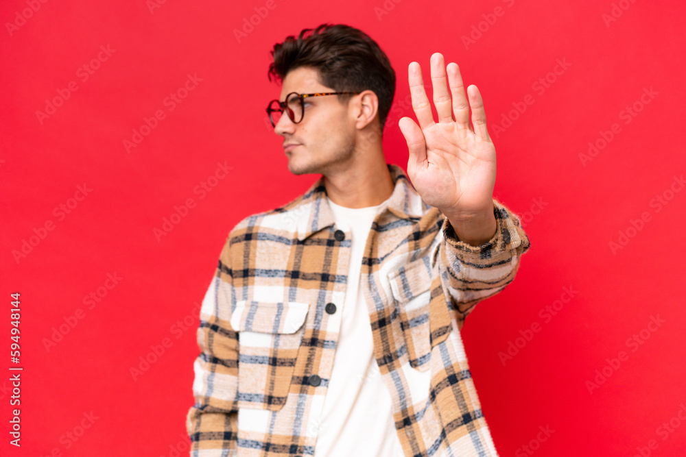 Young caucasian handsome man isolated on red background making stop gesture and disappointed Young caucasian handsome man isolated on red background making stop gesture and disappointed