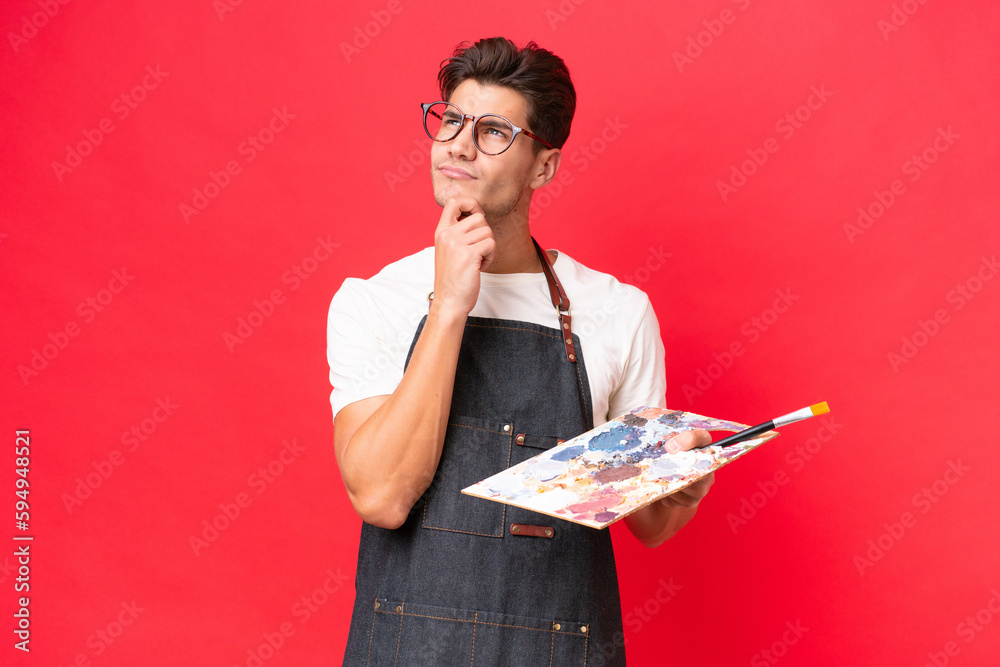 Young artist caucasian man holding a palette isolated on red background having doubts Young artist caucasian man holding a palette isolated on red background having doubts