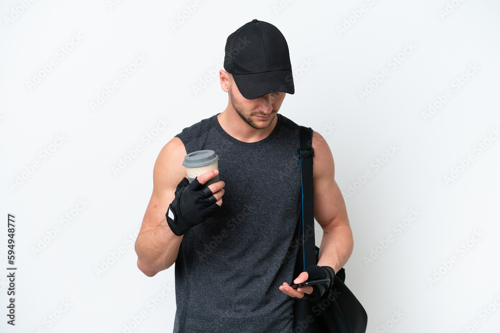 Young blonde sport caucasian man with sport bag over isolated white background holding coffee to take away and a mobile Young blonde sport caucasian man with sport bag over isolated white background holding coffee to take away and a mobile