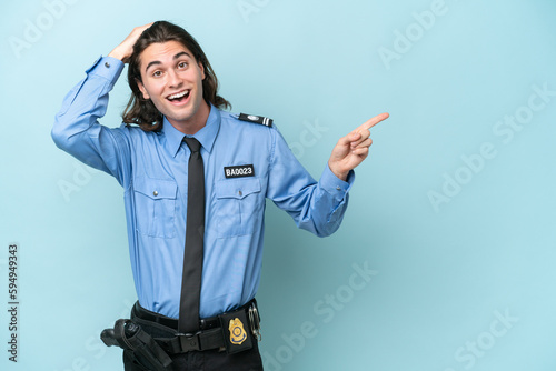 Young police caucasian man isolated on blue background surprised and pointing finger to the side © luismolinero