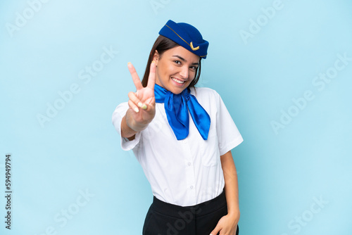 Airplane stewardess caucasian woman isolated on blue background smiling and showing victory sign