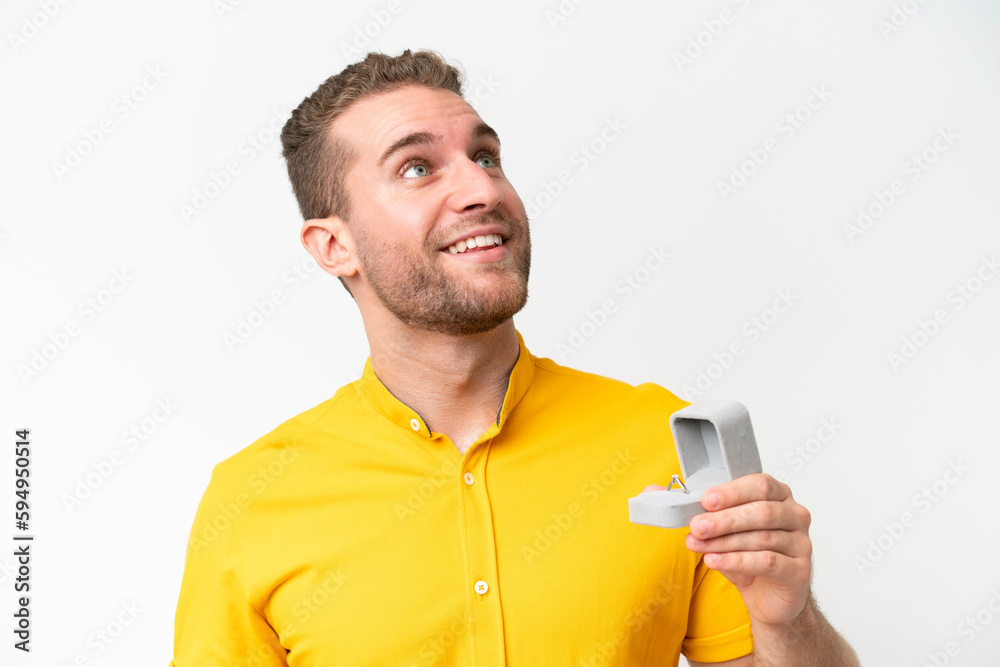 Young man holding a engagement ring isolated on white background looking up while smiling Young man holding a engagement ring isolated on white background looking up while smiling