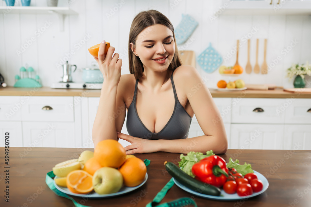 Young and pretty woman sitting at the table full of fruits and vegetables in the wooden interior. Food and health care concept