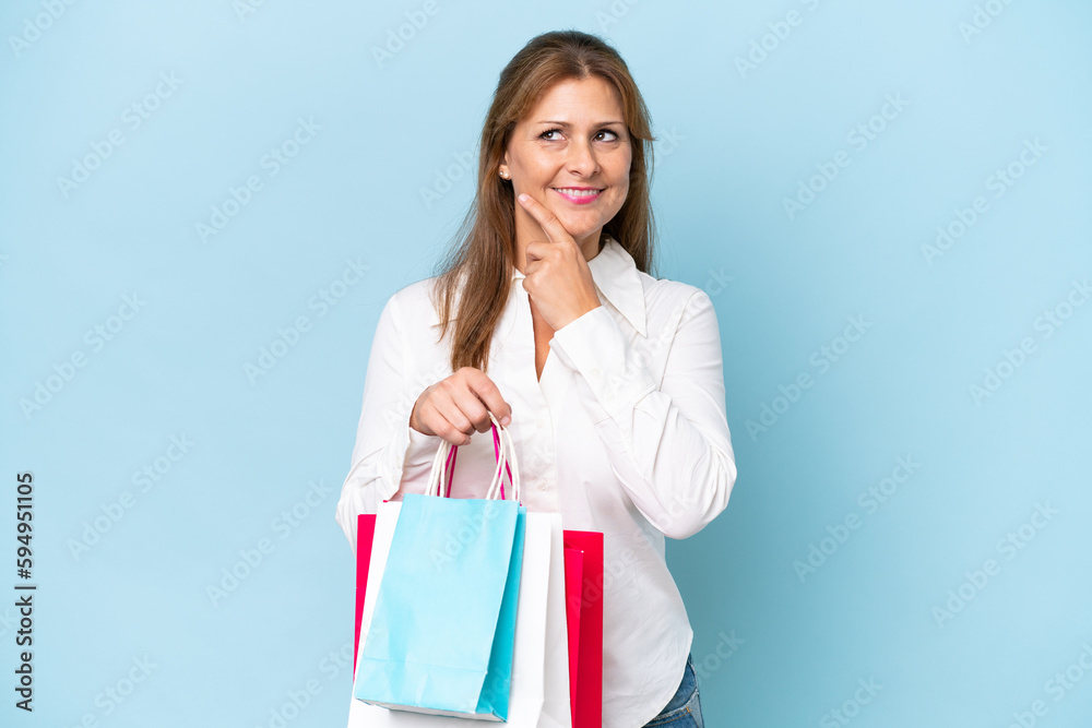 Middle-aged caucasian woman isolated on blue background holding shopping bags and thinking Middle-aged caucasian woman isolated on blue background holding shopping bags and thinking