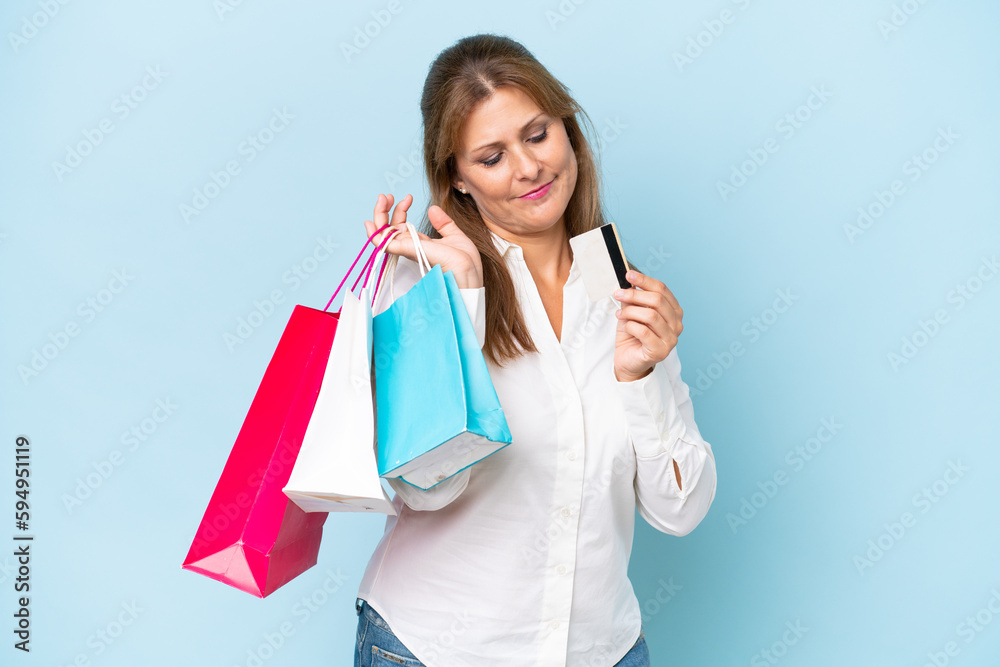 Middle-aged caucasian woman isolated on blue background holding shopping bags and a credit card Middle-aged caucasian woman isolated on blue background holding shopping bags and a credit card