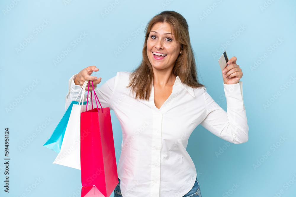 Middle-aged caucasian woman isolated on blue background holding shopping bags and surprised Middle-aged caucasian woman isolated on blue background holding shopping bags and surprised