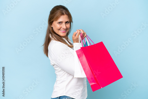 Middle-aged caucasian woman isolated on blue background holding shopping bags and smiling
