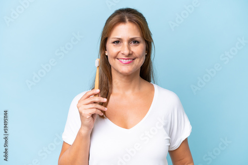 Middle-aged caucasian woman brushing teeth isolated on blue background smiling a lot