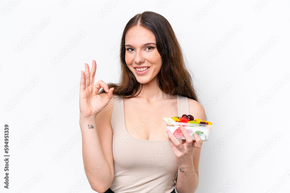 Young caucasian woman holding a bowl of fruit isolated on white background showing ok sign with fingers Young caucasian woman holding a bowl of fruit isolated on white background showing ok sign with fingers