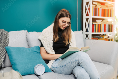 Shocked young woman with watch and laptop sitting on sofa at home