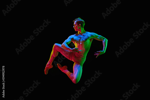 Portrait of one young handsome dancer, actor with naked torm jumping up over dark studio background with neon light. Unusual pose