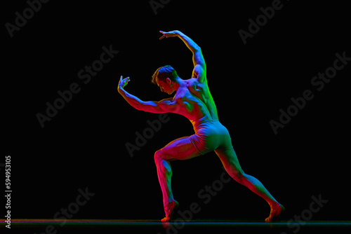 Athletic ballet dancer in a perfect shape performing over dark studio background with neon light. Strength, power