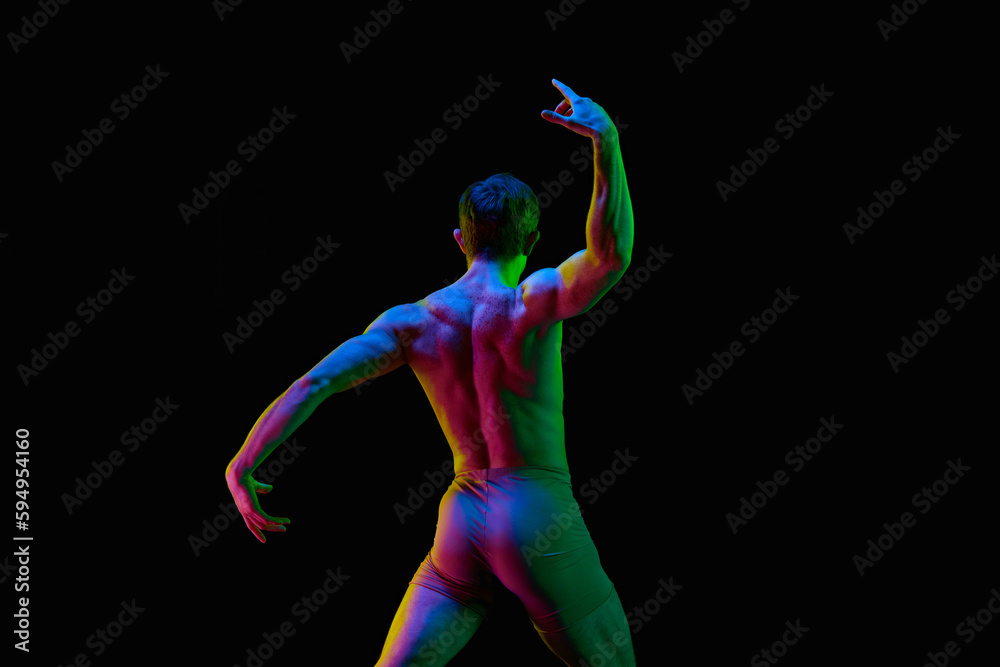 Portrait of one young attractive dancer, actor with naked torm posing over dark studio background with neon light. Back view. Unusual pose