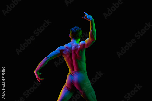 Portrait of one young attractive dancer, actor with naked torm posing over dark studio background with neon light. Back view. Unusual pose