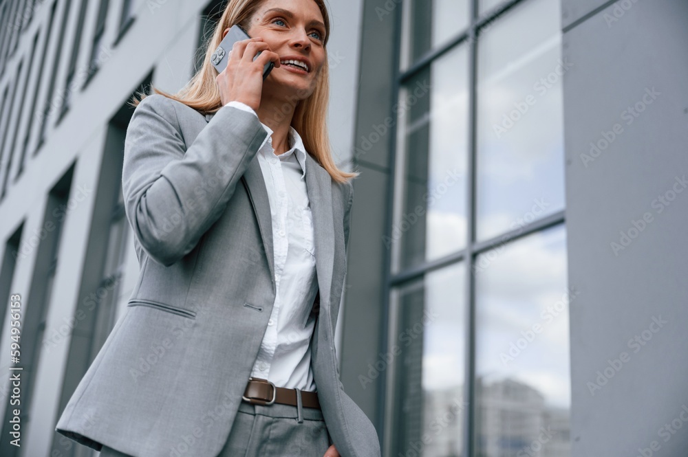 Conversation by the phone. Woman in formal clothes is outdoors near the business building Conversation by the phone. Woman in formal clothes is outdoors near the business building