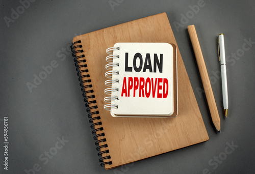 LOAN APPROVED text on notebook with pen and pencil on grey background