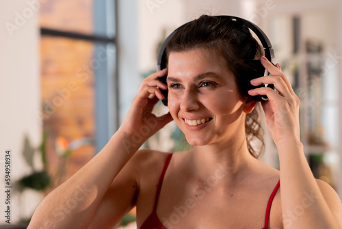 Smiling young woman in tank top listening music in headphones. Sporty girl enjoying song