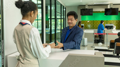 Businessman presents passport and ticket to young female ground staff at airport boarding counter before taking flight. Passenger service at the terminal.