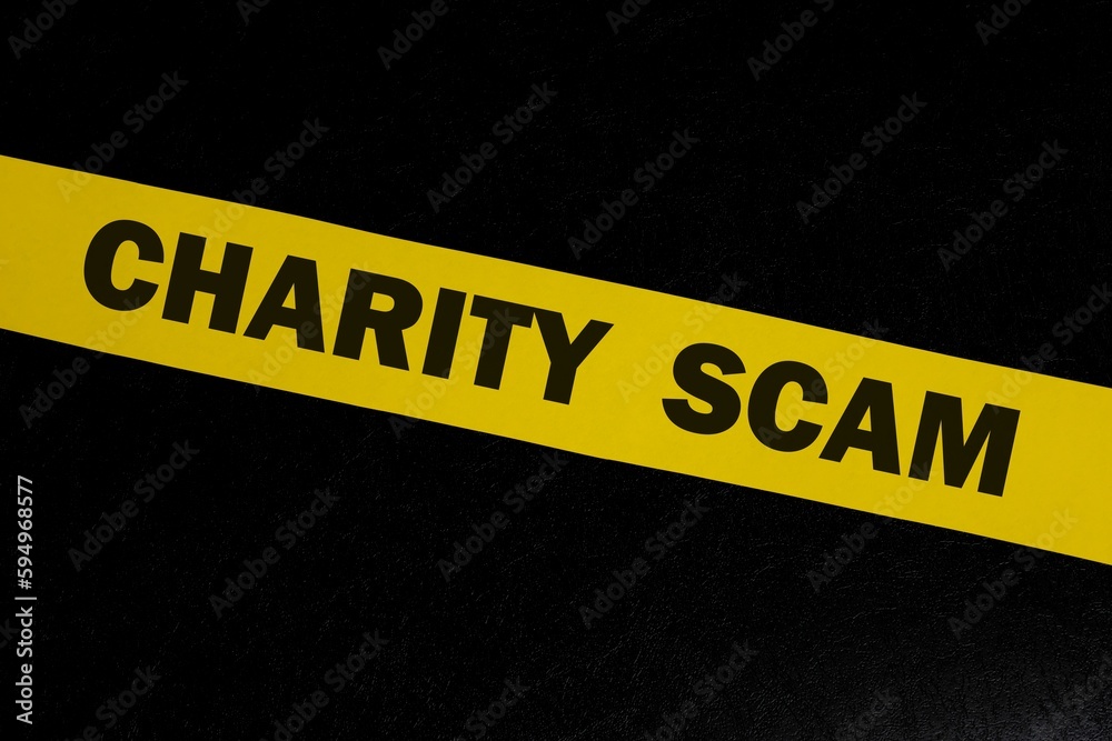 Charity and donation scam and fraud alert, caution and warning concept. Yellow barricade tape with word in dark black background.