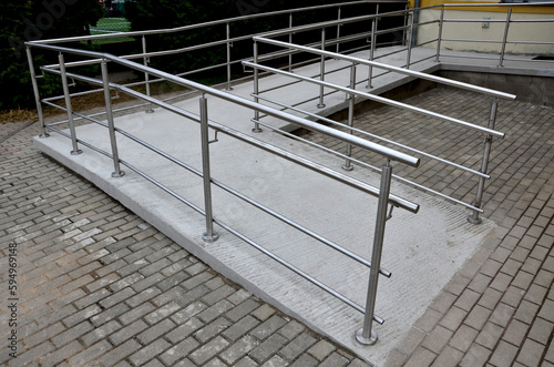 the curved ramp at the entrance to the building is suitable for wheelchair access and supply to the building. stainless steel railing, concrete surface photo