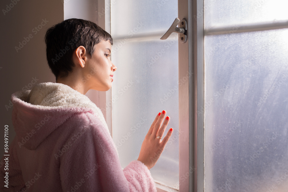 Young woman cancer patient standing in front of a hospital window Young woman cancer patient standing in front of a hospital window