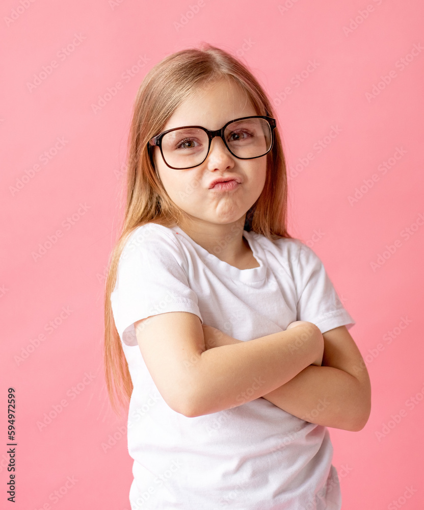 Portrait of a child girl in glasses and a white T-shirt, pink background