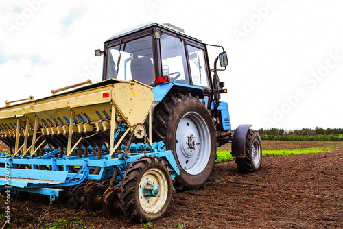 A farmer with a sowing tractor - sowing crops on an agricultural field. Plants  wheat. Early spring  cloudy day. The concept of agriculture