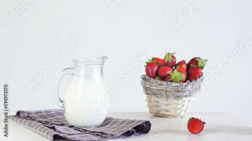 Lactose-free milk in a glass jug and strawberries in a wicker basket