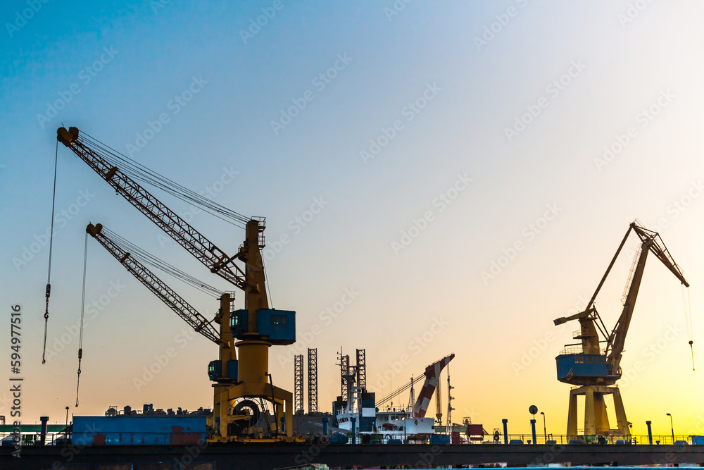 Silhouettes of harbor cranes at sunset. Shipyard at sunset.