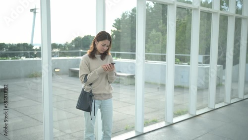 建物の窓ガラスの前でスマートフォンを使う若い女性
