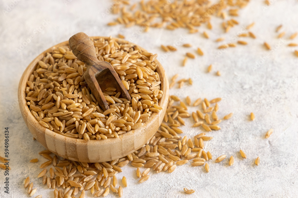Bowl of raw dry rye grain with a wooden spoon on white table close up Bowl of raw dry rye grain with a wooden spoon on white table close up