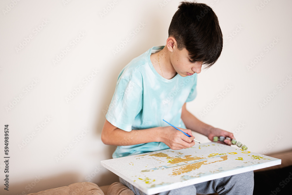 Young male teenager painting picture by numbers on canvas in living room at home. Hobby and leisure concept. Young male teenager painting picture by numbers on canvas in living room at home. Hobby and leisure concept.