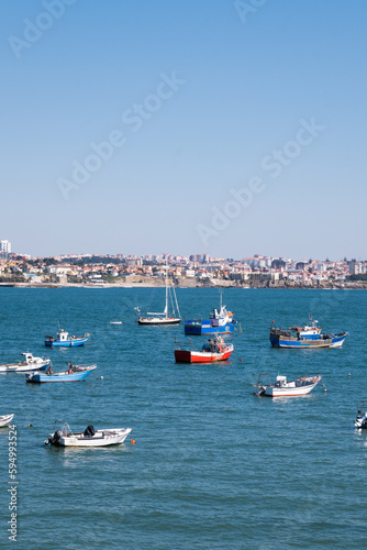 Group of colored boats in the blue waters of the coast of Cascais, Portugal with the city on the horizon