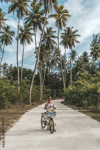 Pretty woman on bicycle on sandy path surrounded with tall palm trees on tropical island
