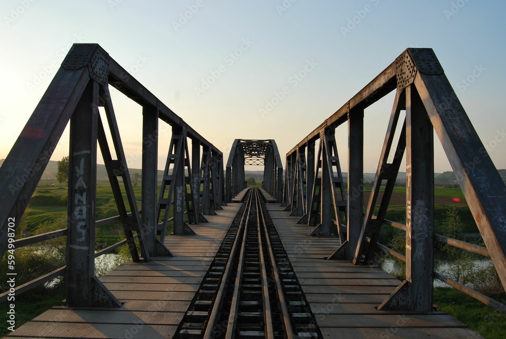 a bridge with rail tracks going across it and grass in the foreground