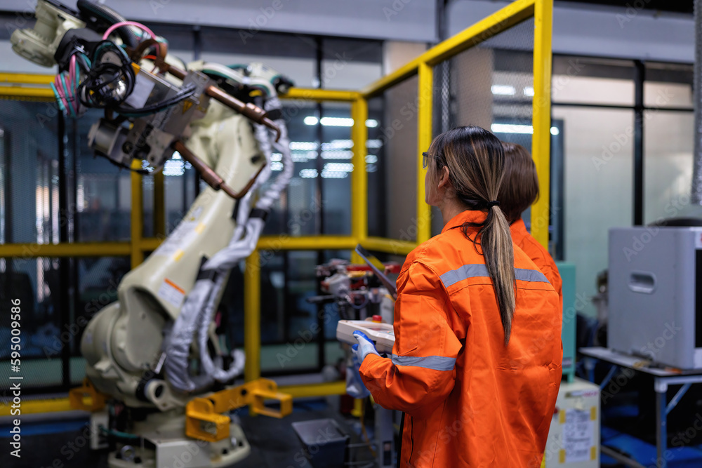 Girl engineer commissioning operating programming and looking at robot machine in the factory Girl engineer commissioning operating programming and looking at robot machine in the factory