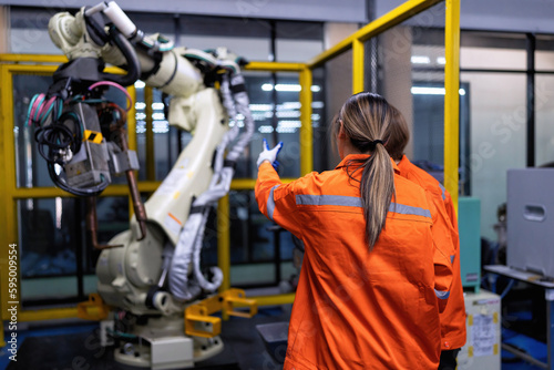 Girl engineer commissioning operating programming and looking at robot machine in the factory