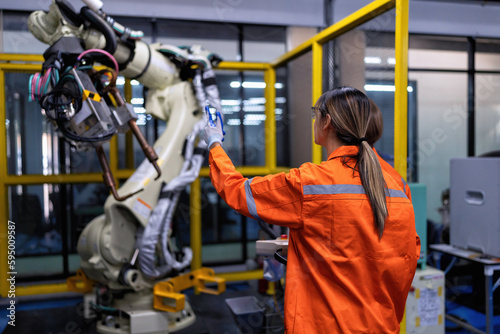 Girl engineer commissioning operating programming and looking at robot machine in the factory