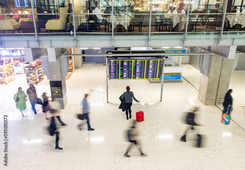 Photography Blurred people walking in an airport hall next to a standing woman reading infor