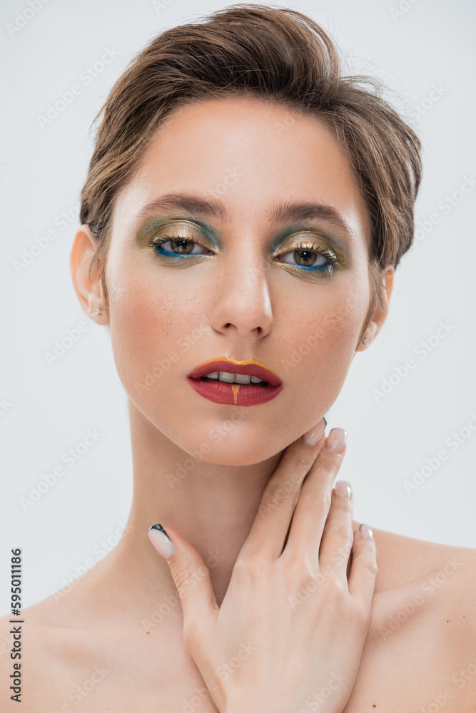 brunette young woman with shimmery eye makeup and red lips touching neck isolated on grey. brunette young woman with shimmery eye makeup and red lips touching neck isolated on grey.