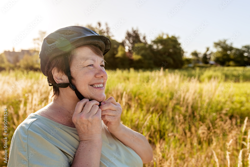 Senior adult plus size smiling woman wearing helmet standing with bicycle outdoors at nature. Healthy active retirement lifestyle and leisure activity Senior adult plus size smiling woman wearing helmet standing with bicycle outdoors at nature. Healthy active retirement lifestyle and leisure activity