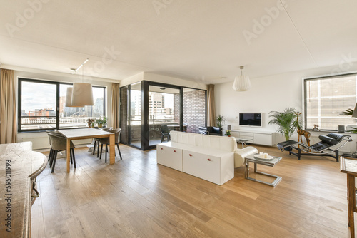 a living room with wood flooring and white furniture in the center of the room is an open kitchen area