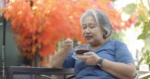 Gray-haired elderly Asian woman sitting and drinking black coffee. To be healthy, stay in cafe with a smile and be happy during the long summer holidays. Concept of taking care of health of senior