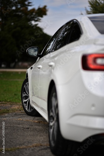 Vertical closeup detail of a white automobile parked in a green setting © Stefan Radosavljevic/Wirestock Creators